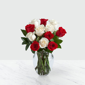 6 red and white roses arranged in a vase with greens on a marble table