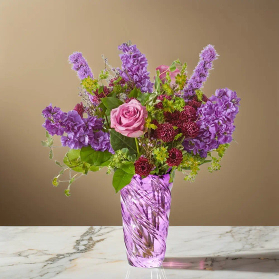 Purple garden style flower arrangement with rose, stock, liatris, scabiosa, and fresh greenery arranged in a purple art glass vase
