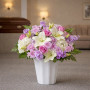 Standard lavender and white sympathy flower arrangement with lilies, roses, hydrangea, and stock displayed in a funeral home setting.