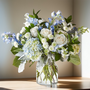 Clearer Skies Bouquet featuring blue delphinium, white roses, and hydrangea arranged in a clear glass vase