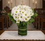 White Daisy Poms arranged in a cylinder vase and greenery in a church