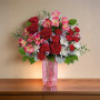 Gorgeous Deluxe Gem Bouquet featuring red roses, carnations, alstroemeria, and white accent flowers arranged in a pink glass vase