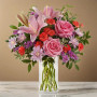 Pink rose and lily flower arrangement with carnations, daisy mums, statice, and greenery in a clear glass vase