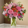 Pink rose and lily flower arrangement with carnations, daisy mums, statice, and greenery in a clear glass vase