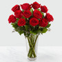 Red roses arranged in a clear glass vase sitting on a white table
