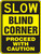 A photograph of a yellow and black 06254 blind corner sign, reading slow blind corner - proceed with caution.