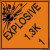 An orange and black photograph of a 03064 dot explosives shipping label, reading explosives 1.3K 1 with graphic.