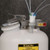 A photograph of a PTFE manifold with a polypropylene fitting, in use.  It is attached to a Justrite HPLC Safety Can and attached to four intake tubes.