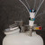 A photograph of a PTFE manifold with a stainless steel fitting attached to a Justrite HPLC Safety Can.  A PTFE manifold with a stainless steel stacker connector is attached to top oof it.  Several intake lines are attached to both manifolds.