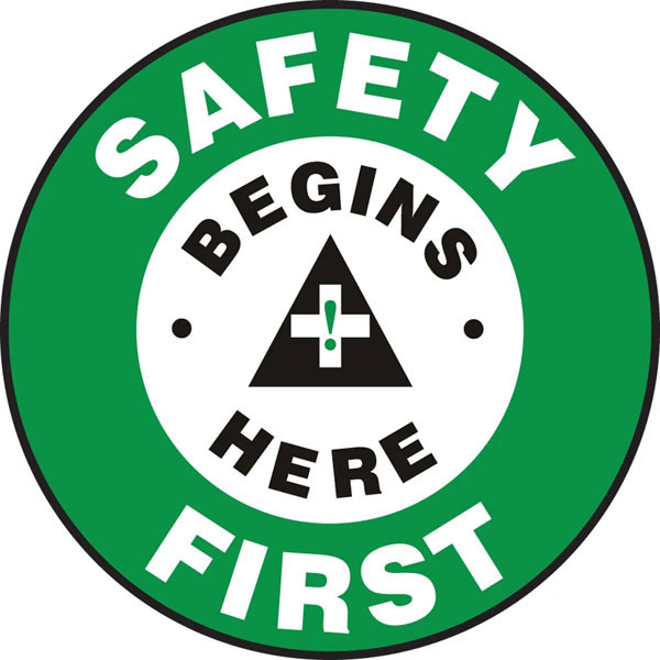 An image of a Slip-Gard™ Floor Sign.  The words "SAFETY FIRST" are in white lettering on green around the circumference of the sign. "BEGINS HERE" is in black lettering on a white circle in the middle of the sign with a with a graphic in the center.