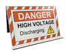 Image of the orange and white high visibility sign features the text: "DANGER HIGH VOLTAGE DISCHARGING", with a yellow electrical discharge symbol, at a 45 degree angle.