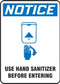 A photograph of a blue and white 03445 OSHA notice sign, reading use hand sanitizer before entering, with icon.