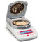Photograph of an Ohaus MB23 Moisture Analyzer, with sample, open, right-facing.