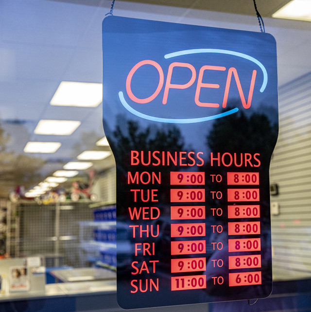 A sign in a store window that reads "Open" and business hours listed.
