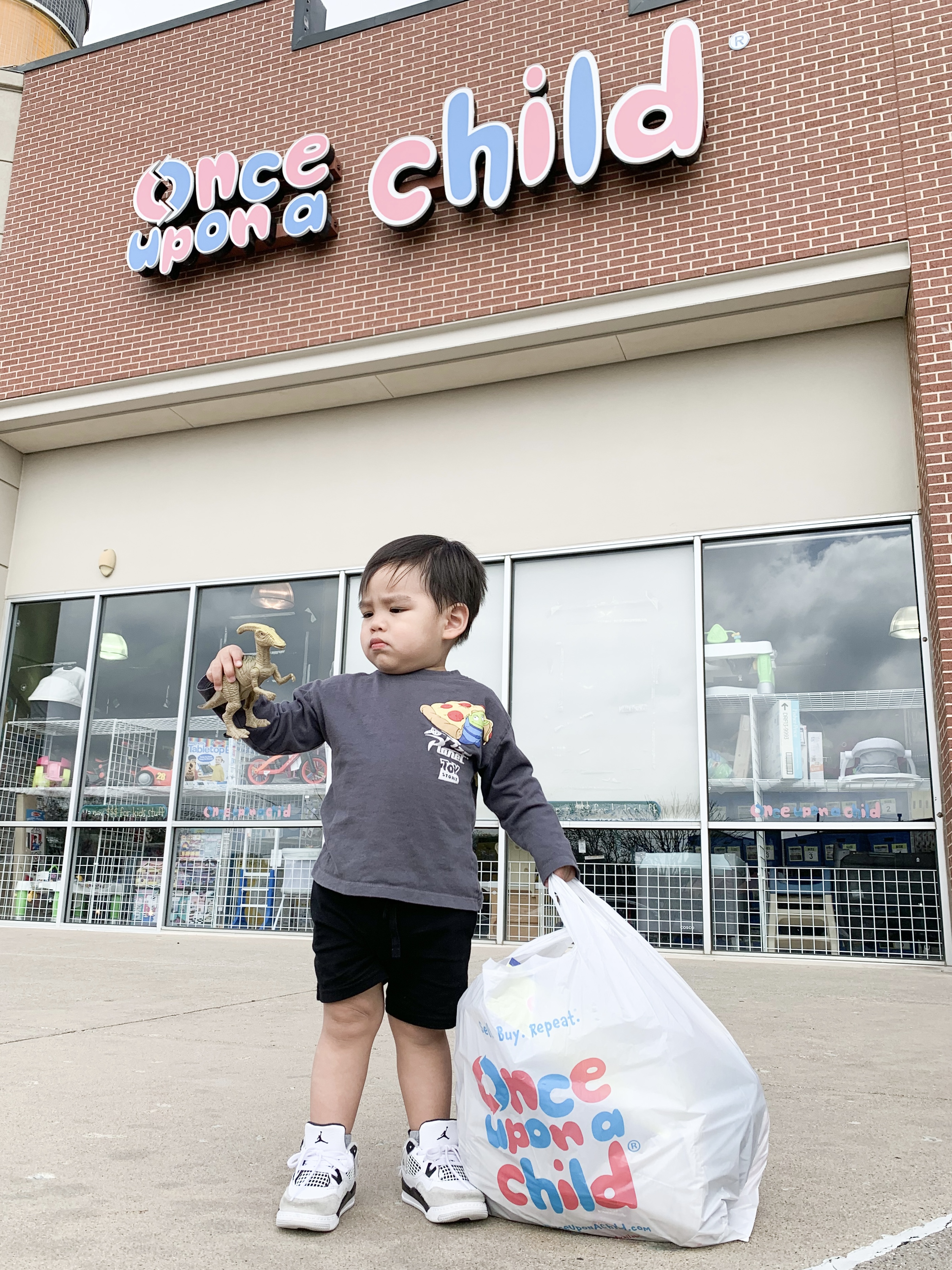 Child standing in store front holding shopping bag