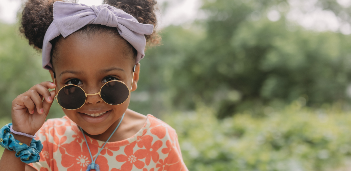 A young girl with sunglasses and a flower headband, radiating joy and style