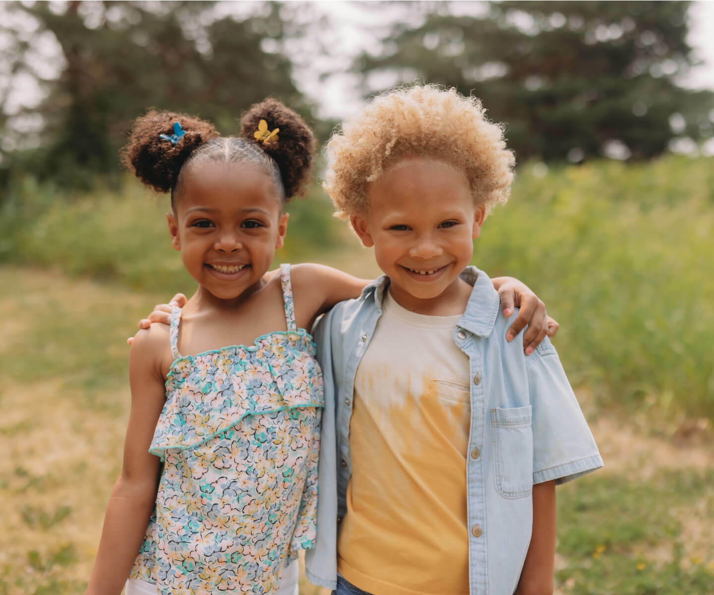 Two young children standing in a field, enjoying the outdoors with hands on shoulders of each other