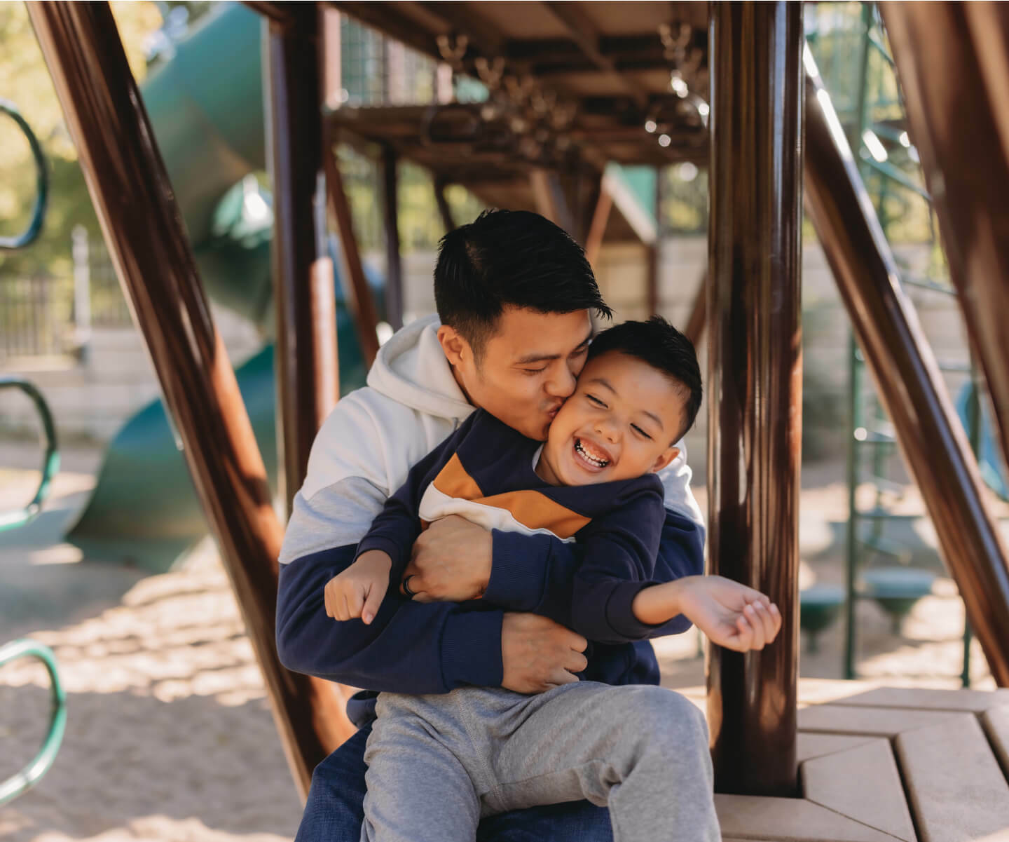 A young men kissing a child on cheek while sitting in a park, both smiling