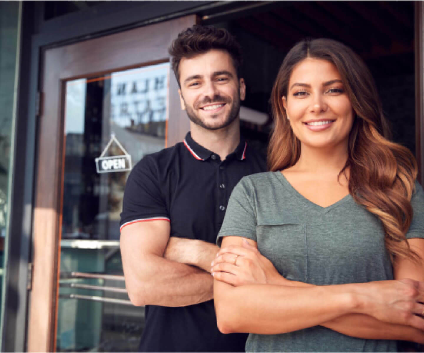 A man and woman standing outside a business with folded arms.