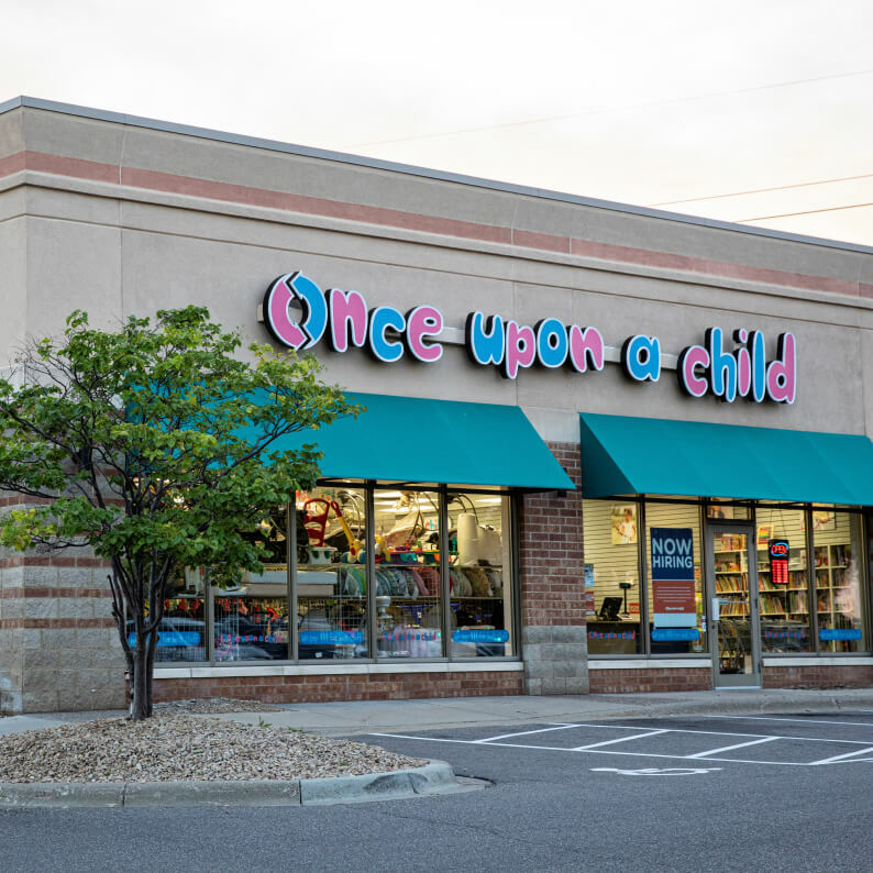 A store front with billboard "Once Upon A Child" and a tree in front of it