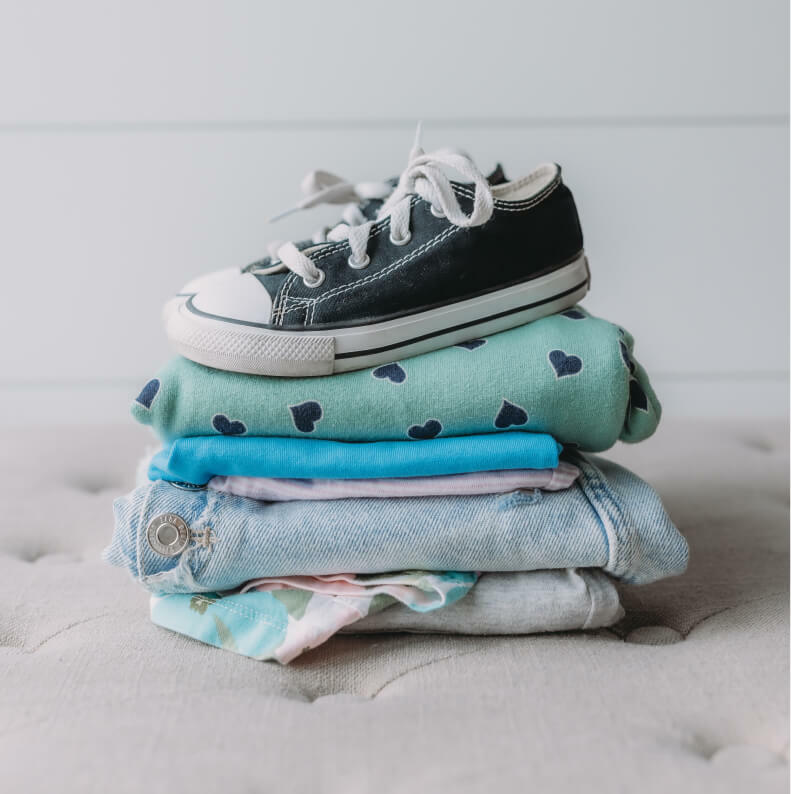 A stack of folded clothes with a pair of sneakers on top