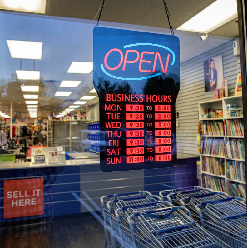 A sign in a store window that reads "Open" and business hours listed.