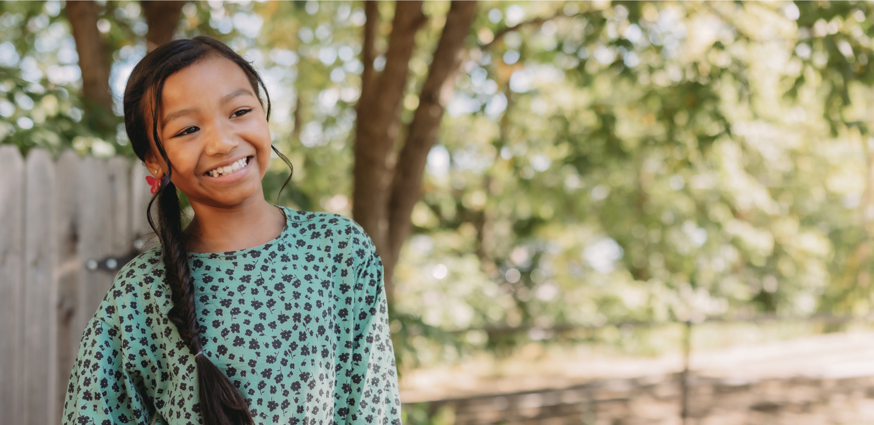 A young girl smiling in front of a tree