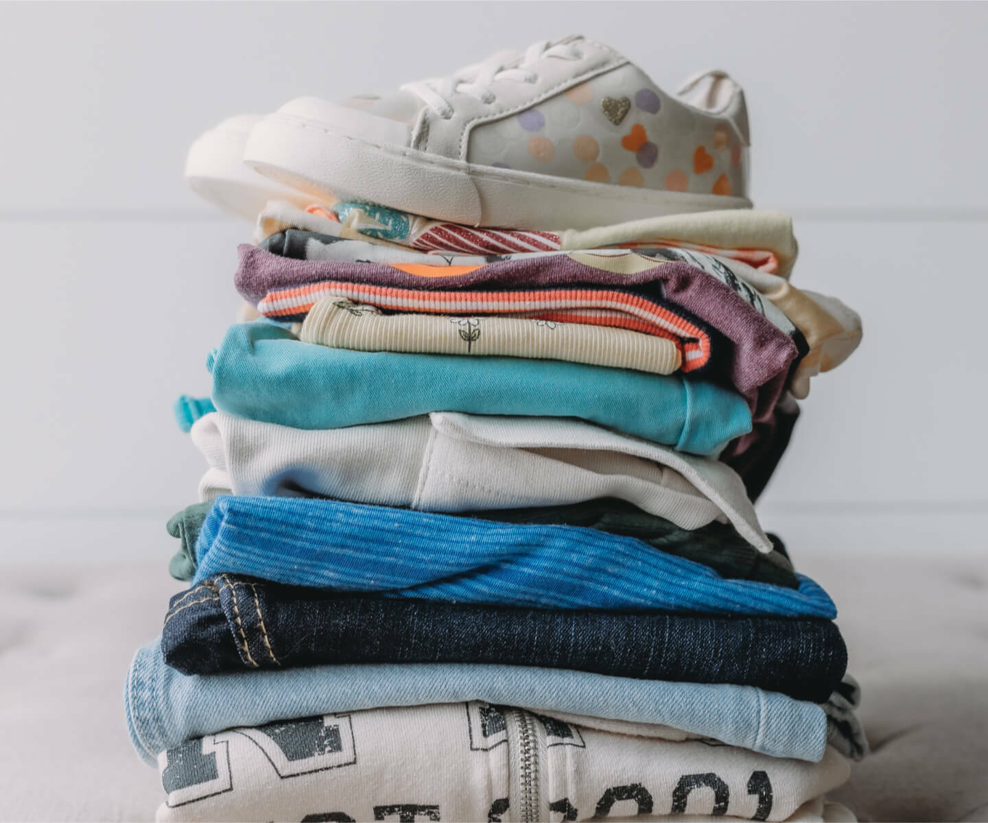 Stack of clothes organized on a bed Image and with sneakers on top 