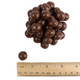Close-up of crunchy brown milk chocolate covered pretzel balls with ruler to show size
