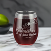 Personalized 15oz stemless wine glass with laser etched fairy godmother design, personalized with godchild name and date. Filled with red wine and placed on a marble surface, this custom glass makes a perfect gift for godmothers on special occasions.
