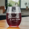 Custom 15oz stemless wine glass featuring a laser etched godmother design, personalized with godchild name and date. Filled with red wine, this personalized glass is perfect for gifting godmothers on special occasions like christenings or birthdays.