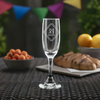 Custom laser-etched stemmed champagne flute with logo design on a wicker table, against a backdrop of festive party flags and a spread of snacks, showcasing a personalized engraving option for special events.