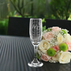 Custom engraved champagne flute with intertwined initials A&D and a date of 07.15.2024, displayed beside a vibrant bouquet of roses and greenery, set on an elegant outdoor patio table, perfect for wedding toasts and couple's gifts.