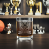 Custom engraved double rocks whiskey glass with a detailed etching of a ram and 'Coach Simmons 2022 Championship Season' text, displayed in front of a trophy case filled with sports awards, ideal for personalized coach gifts and sports memorabilia collectors.