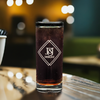 Customized 10.5 oz highball glass with 'J&J DESIGNZ' etching, presented on a bar countertop with ambient bokeh lighting in the background, perfect for personalized corporate gifts or sophisticated barware.