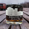 Custom laser-etched 11oz whiskey glass featuring Scranton, PA skyline and 'The Electric City' text, displayed on a rustic wooden surface, highlighting custom city-themed glassware design.