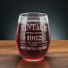 A personalized 15oz stemless wine glass filled with red wine, featuring a laser etched Vintage Aged to Perfection design with personalized year and text line. The glass rests on a wooden surface, perfect for milestone birthday gifts.