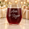 Back of a stemless wine glass with two lines of personalized script text, displayed with wrapped gifts and warm celebration lights.
