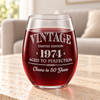 Close view of a vintage stemless wine glass with a personalized year and bottom line of script text on a stone table.