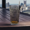 Etched Columbus, Ohio street map pint glass, set against an urban backdrop with Columbus skyline, highlighting the Ohio State University area on a wooden surface, ideal for gifts and memorabilia for OSU students, alumni, and city enthusiasts.