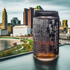 Etched Columbus skyline and street map on a 16 oz can glass, foregrounded against the panoramic cityscape and Scioto River, an ideal souvenir for Columbus visitors or a treasured gift for residents and Ohio State University enthusiasts.