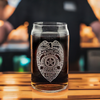 Personalized correction officer badge engraved on a 16 oz Libbey beer can glass, displayed on a bar counter, perfect for law enforcement officers' gifts and memorabilia
