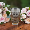 Customizable etched pint glass with Celtic Tree of Life design, personalized with name. Ideal for weddings, anniversaries, and special occasions. Shown with a beverage, cake, and flowers, perfect for gifting or personal use.