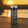 Black 22oz stainless steel tumbler with a personalized Maltese cross design. The tumbler is placed on a wooden table overlooking a serene sunset by the water, ideal for firefighter gifts.
