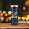 Navy blue 22oz stainless steel tumbler with optional backside text laser etched. The tumbler sits on a wooden surface with a blurred, warm toned background featuring bokeh lights.