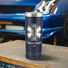 Navy blue 22oz stainless steel tumbler with a silver EMT paramedic star of life symbol laser etched on the front. The design is personalized with two lines of text. The tumbler sits on a surface in front of a blue car background.