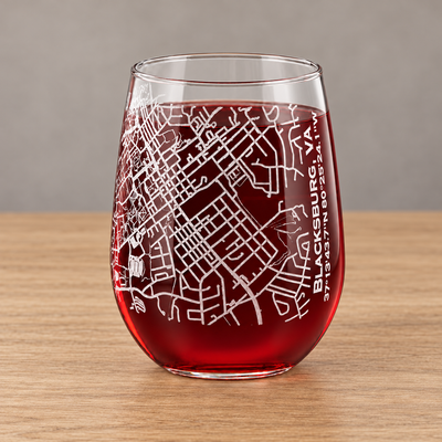 Blacksburg Virginia street map etched on a stemless wine glass filled with red wine, on a wood table against a neutral background