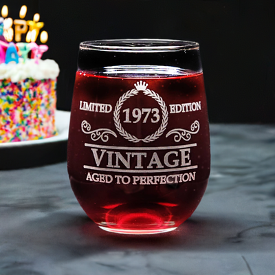 Custom-engraved stemless wine glass, featuring the text 'Limited 1973 Edition Vintage Aged to Perfection' with a colorful birthday cake and lit candles.