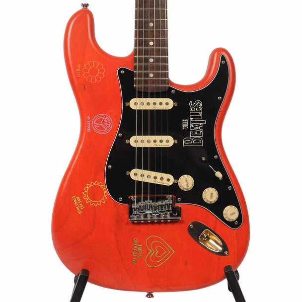 Close front view of Coyle S-style electric guitar in Fiesta Orange with black Beatles-themed pickguard, three cream single-coil pickups, and colorful peace and love graphics. card