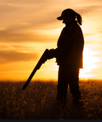 Silhouette of a woman holding a shotgun at sunset